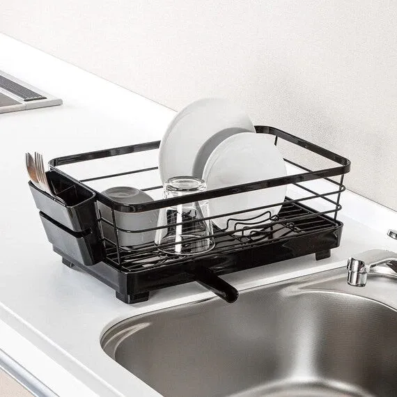 NITORI black double-coated slim single-tier dish drainer beside a sink with plates, a glass and a side cutlery caddy, angled view